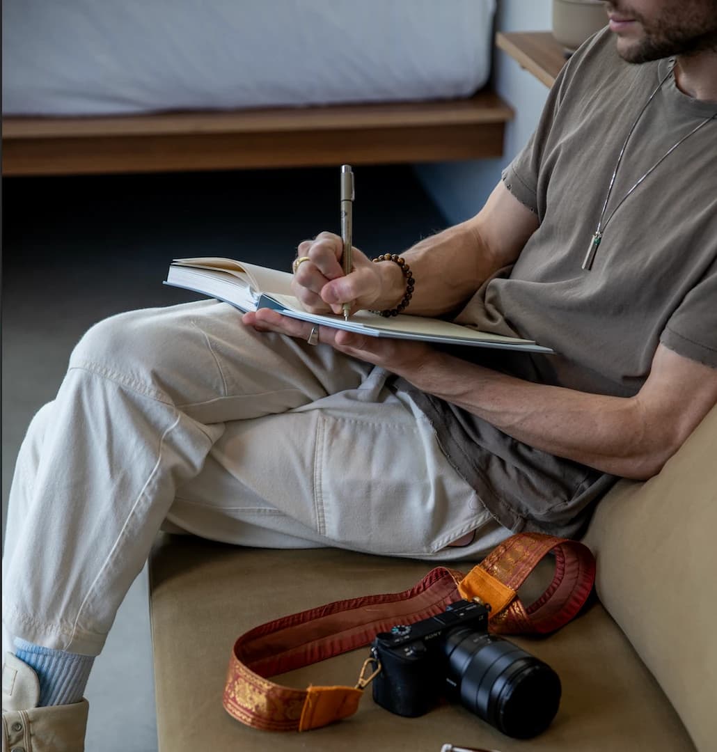 A person journaling on a sofa, with a camera beside them